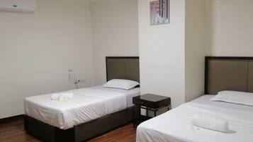 A hotel room with two single beds, a small bedside table, a wall-mounted air conditioner, and a framed picture on the wall.