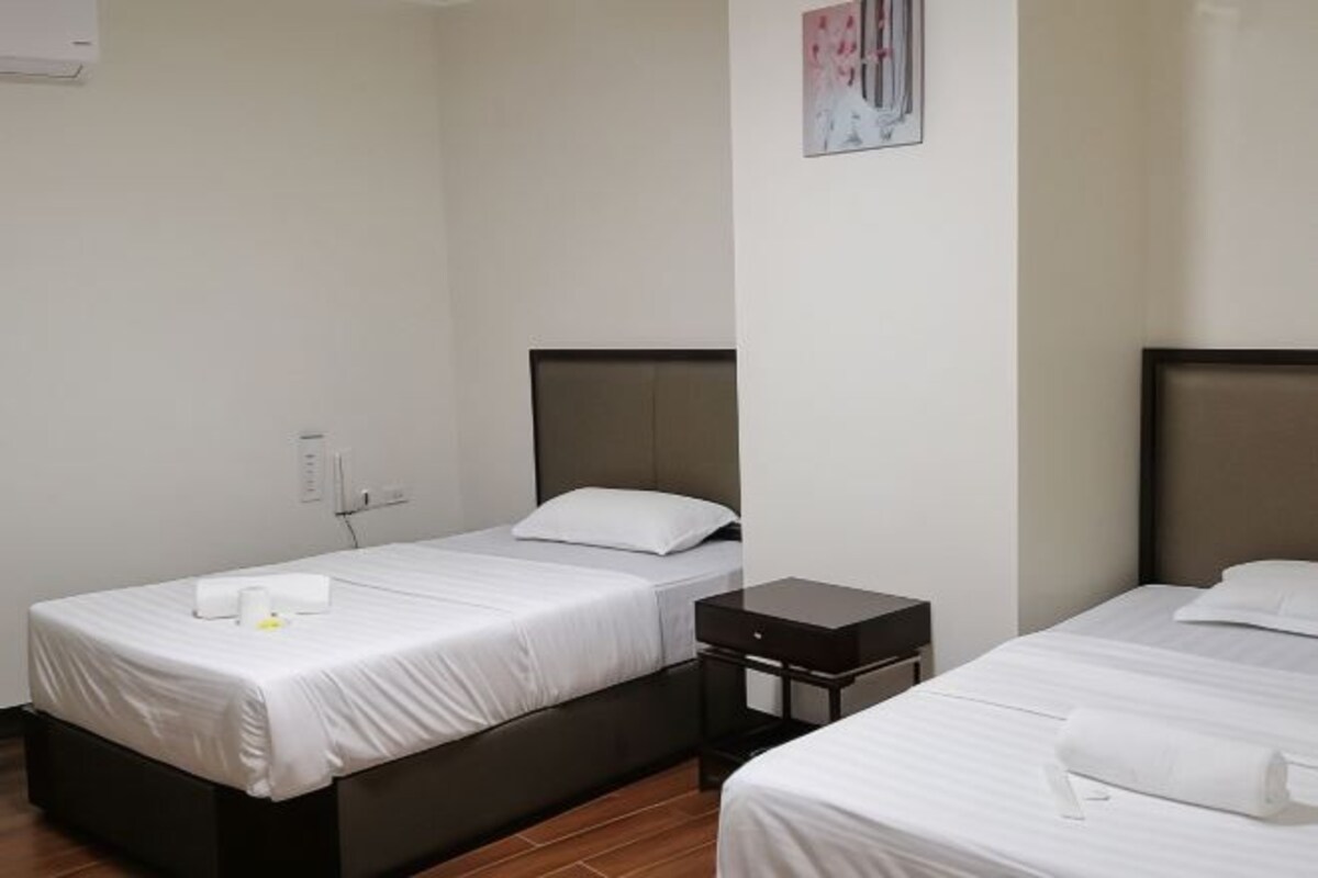 Habitación de hotel con dos camas individuales, una mesita de noche pequeña y un equipo de aire acondicionado instalado en la pared.