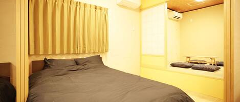 A bedroom with a bed, curtains, an air conditioning unit, a mirror, and a bench with pillows.
