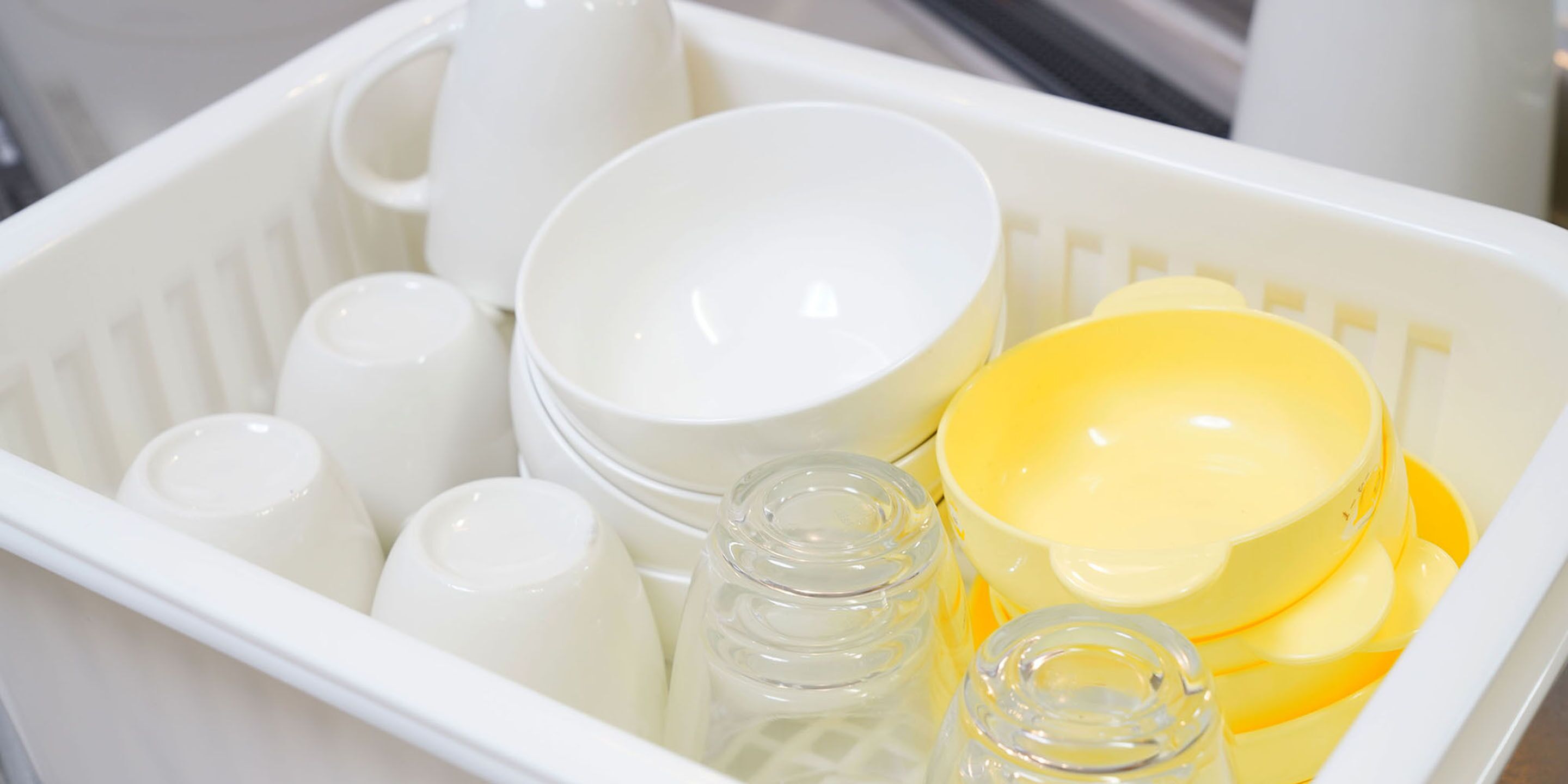 A white plastic basket containing various kitchenware items including cups, bowls, and jars.