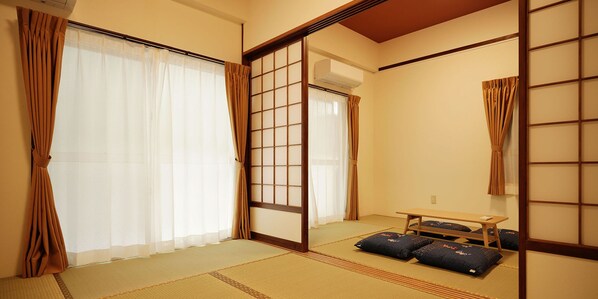 Una habitación japonesa tradicional con suelo de tatami, puertas correderas, una pequeña mesa y cojines.