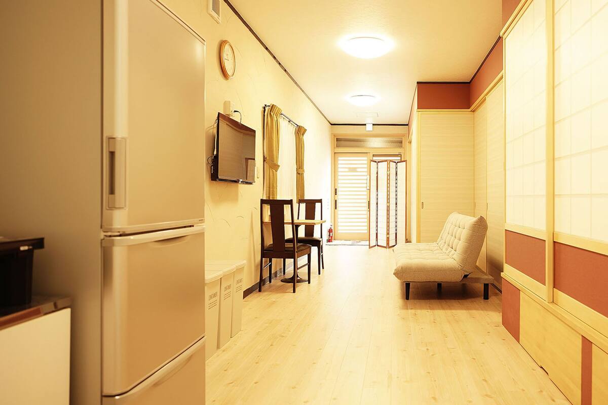 A hallway with a refrigerator, a chair, a table, and a cushioned bench.