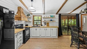 A kitchen with white cabinets, a wooden countertop, a black refrigerator, and a hanging light fixture. - Creekside Cabin~Jacuzzi~fire pit~screened porch (Cosby)