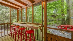 A wooden deck with a bar area, red stools, and a view of a forested area. - Creekside Cabin~Jacuzzi~fire pit~screened porch (Cosby)