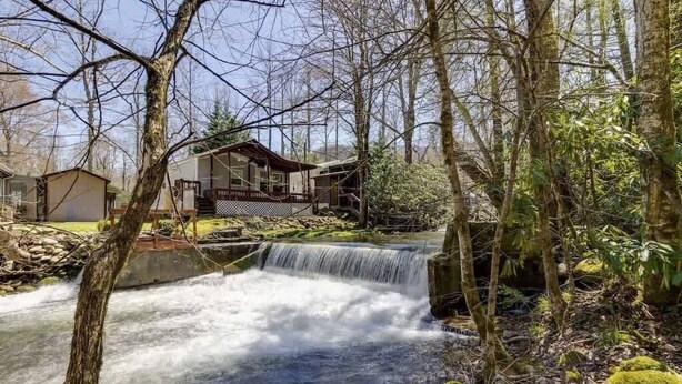 A waterfall in a forested area with a house in the background. - Creekside Cabin~Jacuzzi~fire pit~screened porch (Cosby)