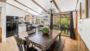 A modern kitchen with a dining area, featuring a large wooden table, black appliances, and a view through a glass door. - Creekside Cabin~Jacuzzi~fire pit~screened porch (Cosby)