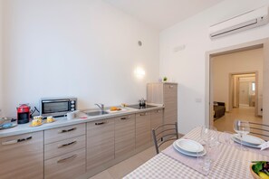 A modern kitchen with a microwave, coffee maker, and sink. There is a dining table set with plates, glasses, and a bowl of fruit. - Suite 1 Ondina Viareggio 200m from sea, Viareggio, Italy (Viareggio)