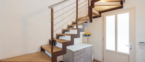 A staircase with wooden steps and metal railings, leading to a landing with a white cabinet and a door with glass panels.