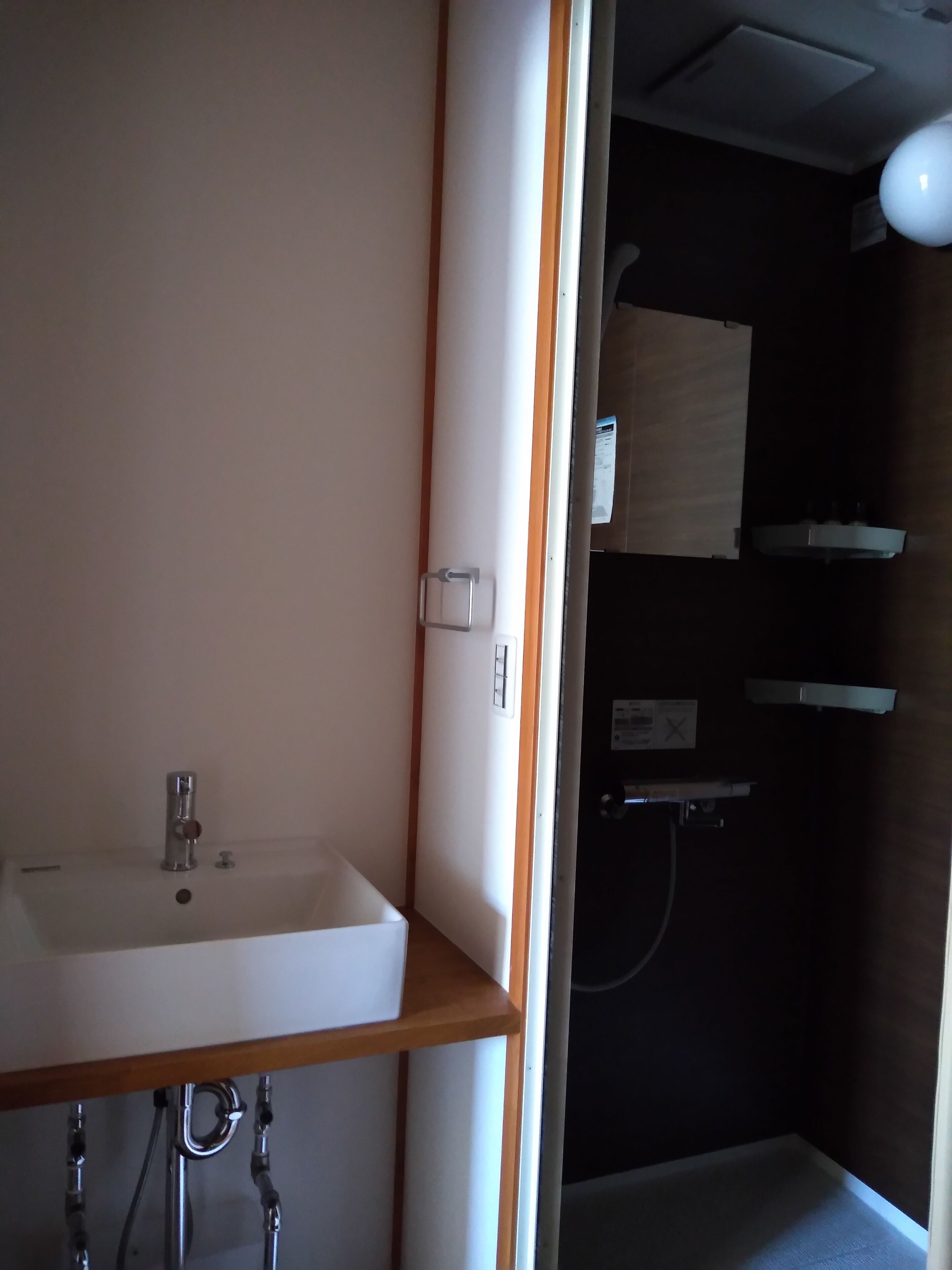 A bathroom with a white sink, wooden vanity, and a shower area.