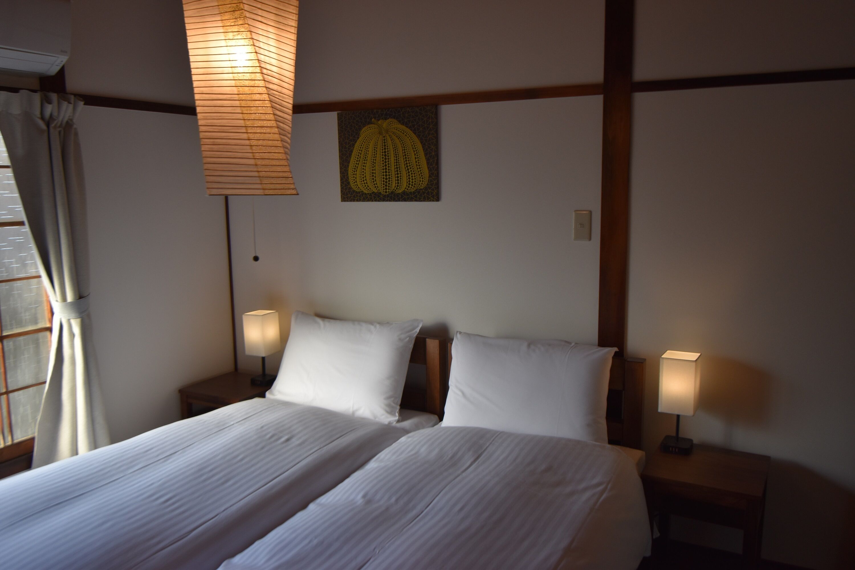 Una camera d'albergo con un letto grande, due comodini con lampade, un'opera d'arte appesa al muro e una finestra con tende.