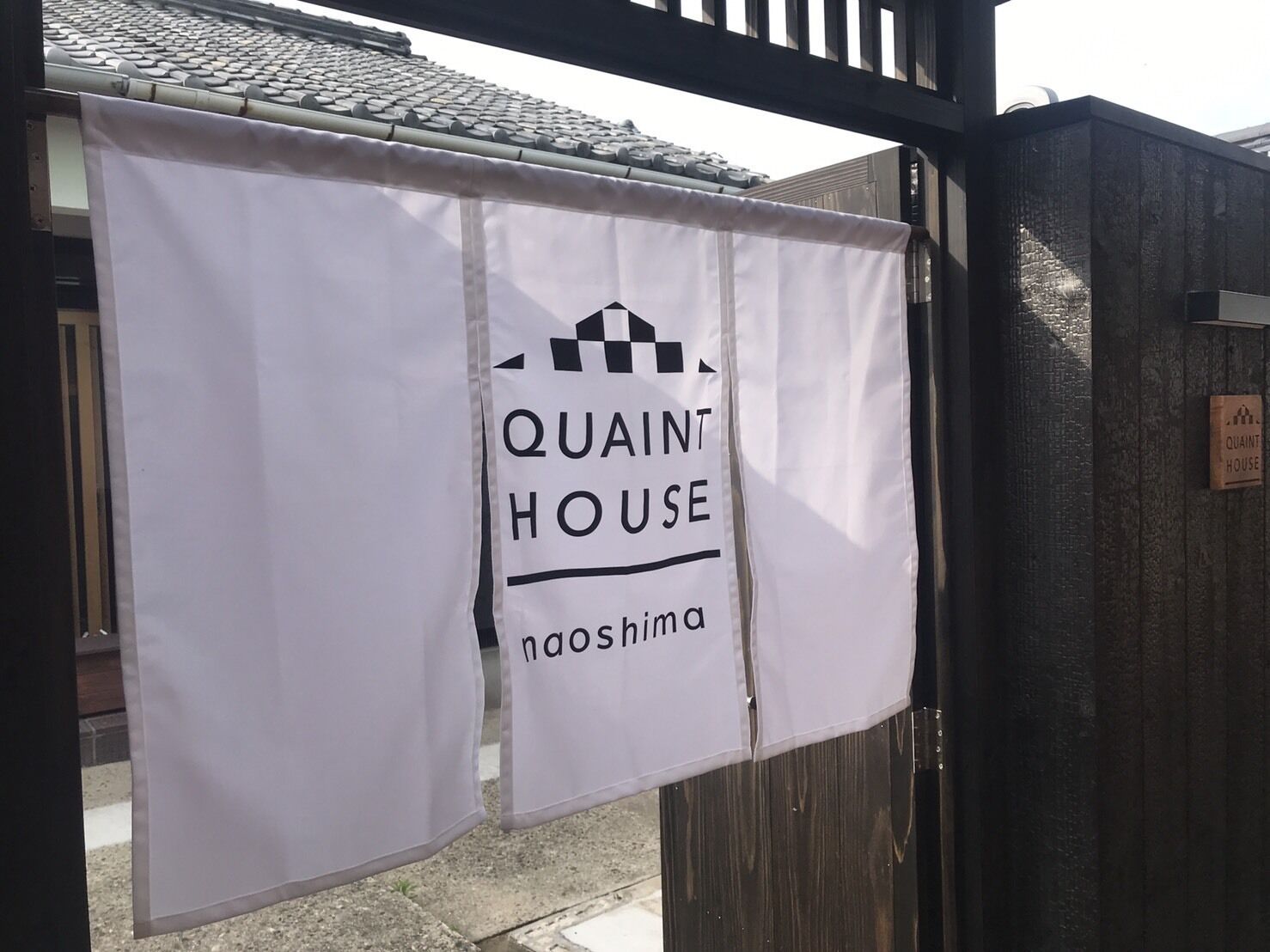 A banner with "QUAINT HOUSE" and "noshima" text, hanging on a gate.