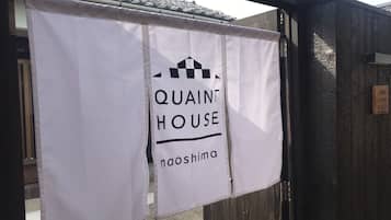 A banner with "QUAINT HOUSE" and "noshima" text, hanging on a gate.