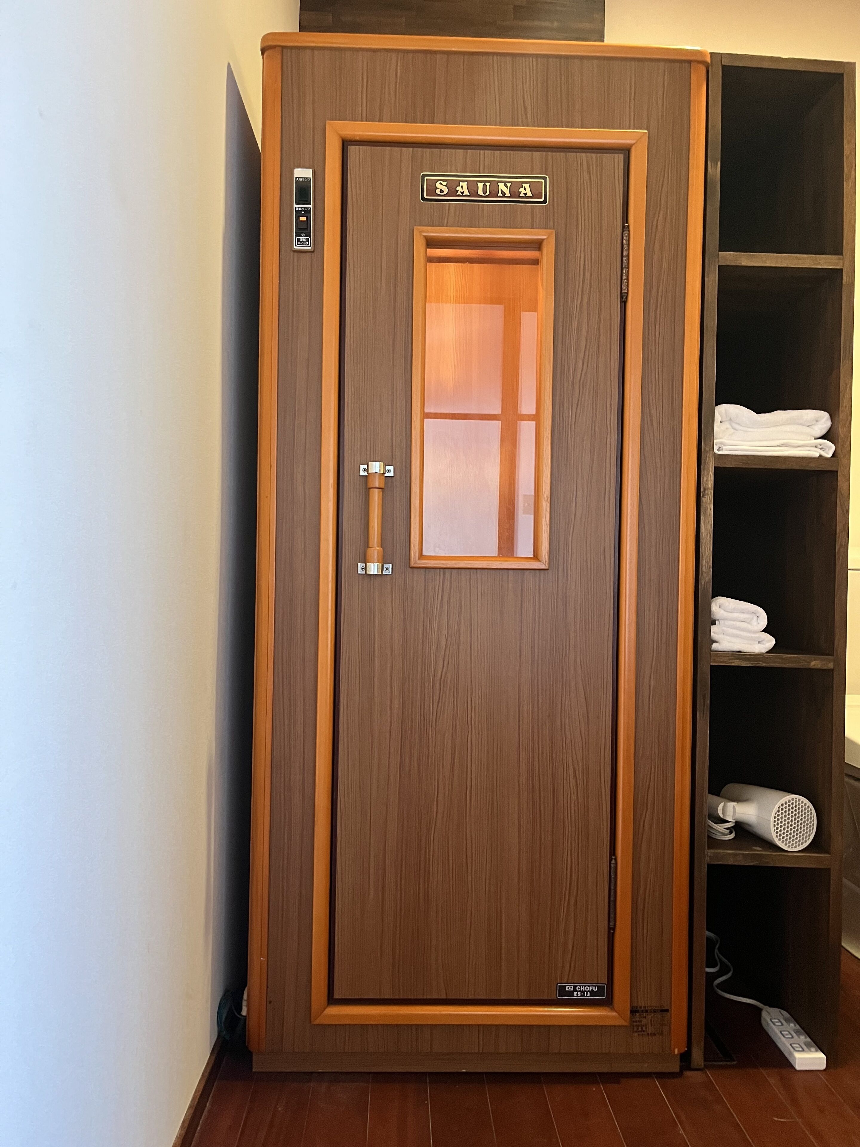 A wooden sauna cabinet with a glass door, a towel rack, and a control panel.