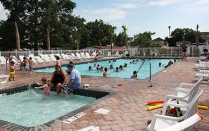 A swimming pool area with multiple pools, lounge chairs, and a brick walkway. - Our Escape Near the Sea! Limo Golf Cart Included (Garden City)