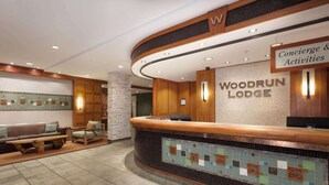 Un área de recepción con un mostrador de madera, una zona de estar con un sofá y sillones, y un diseño de mosaico en el suelo.