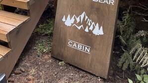 A wooden sign with "WOOLLY BEAR CABIN" and a mountain graphic, located at a cabin entrance with wooden stairs and a deck. - Woolly Bear Log Cabin Mountain Get-Away (Packwood)