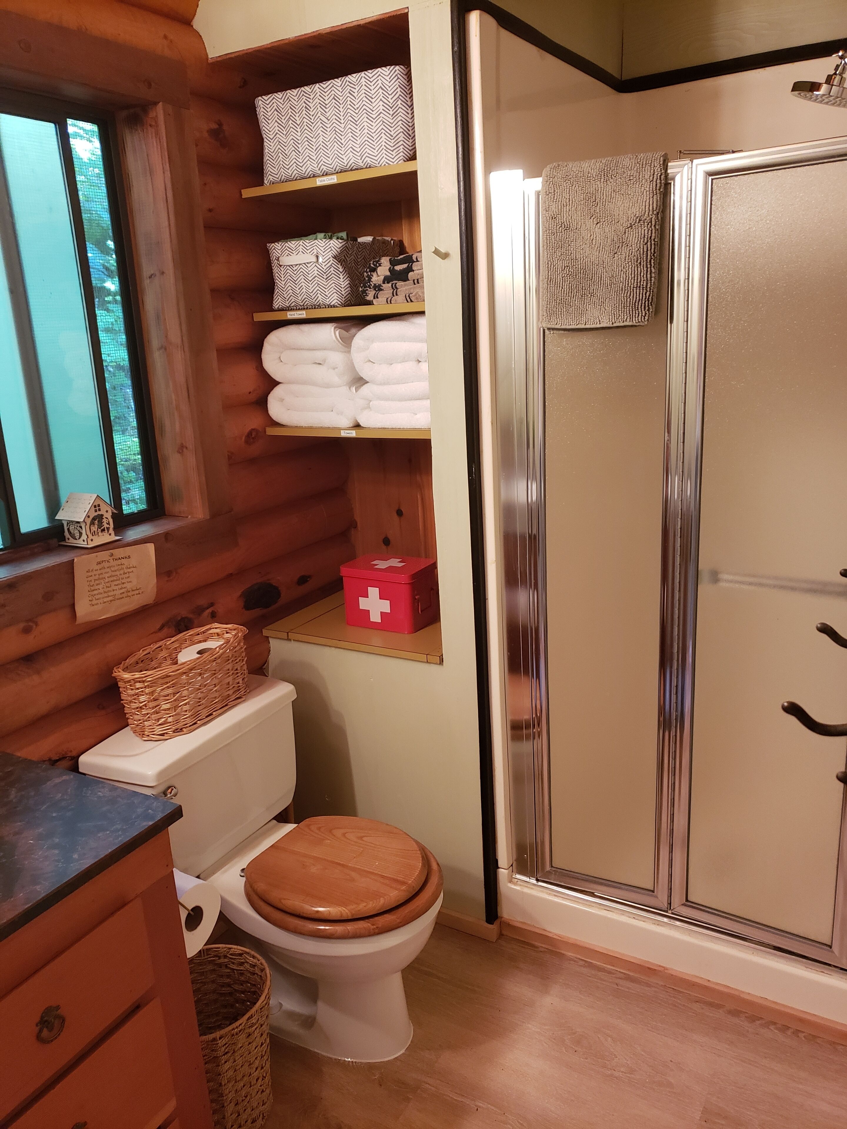 Un baño con diseño tipo cabaña de madera, que incluye un inodoro, una ducha y un estante con toallas y un botiquín.