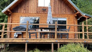 A wooden cabin with a balcony, a table, and chairs. - Woolly Bear Log Cabin Mountain Get-Away (Packwood)