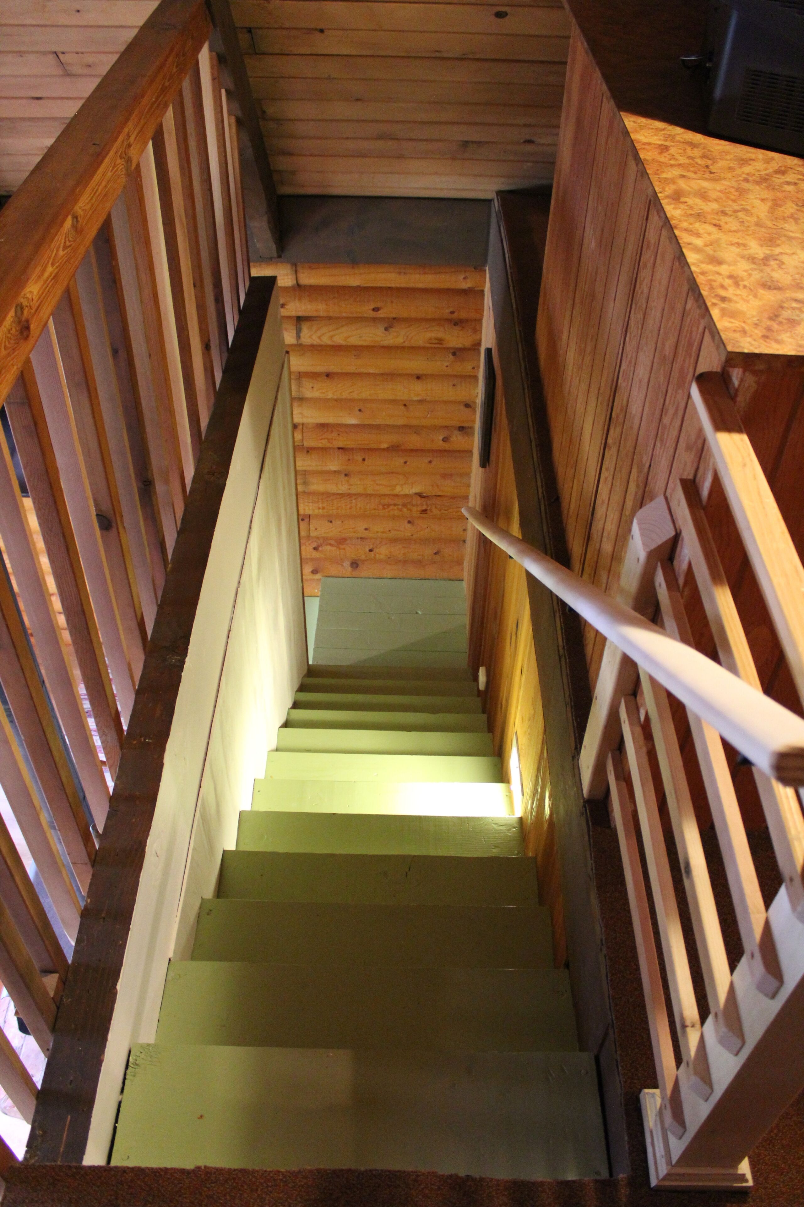 Una escalera de madera con barandilla, que conduce a una habitación con paredes y techo de madera.