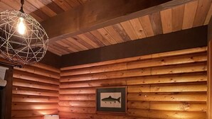 A log cabin bedroom with a bed, checkered pillows, a framed fish picture, and a hanging light fixture. - Woolly Bear Log Cabin Mountain Get-Away (Packwood)