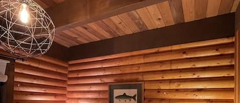 A log cabin bedroom with a bed, checkered pillows, a framed fish picture, and a hanging light fixture.