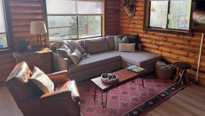 A cozy log cabin interior with a sofa, armchair, and a dining table. - Woolly Bear Log Cabin Mountain Get-Away (Packwood)
