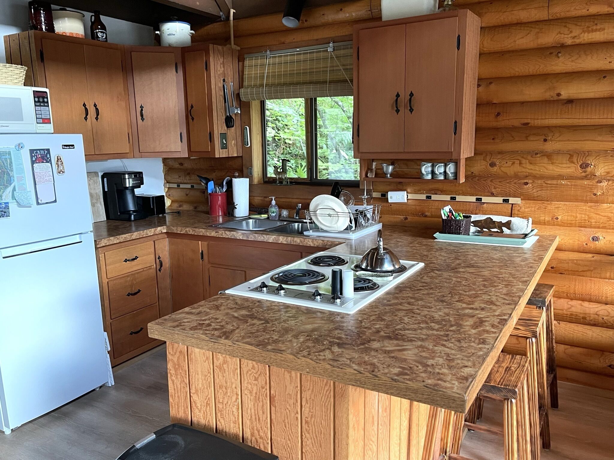 A wooden cabin kitchen with a central island, a refrigerator, a stove, and a sink.