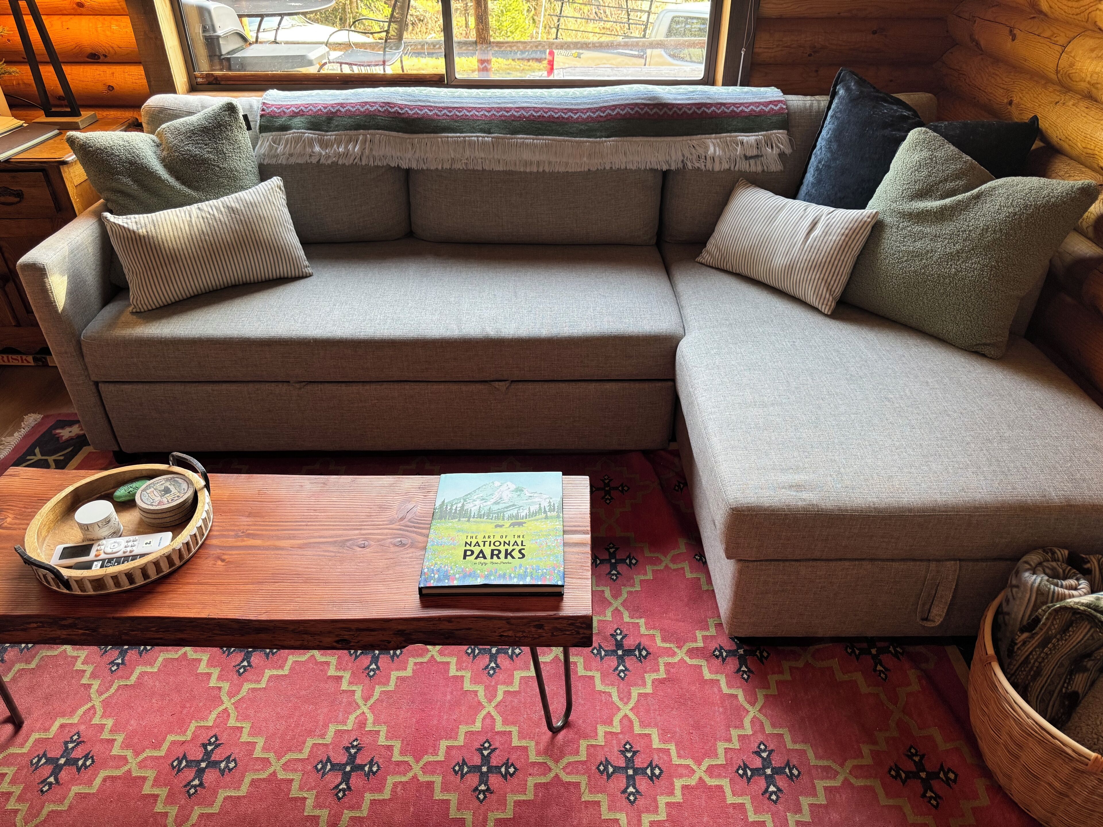 A cozy living room with a sectional sofa, a wooden coffee table with a book titled "The Art of the National Parks," and a patterned rug.