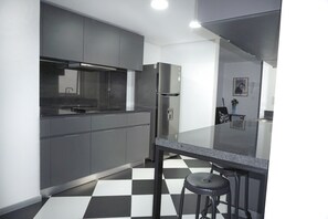 A modern kitchen with grey cabinets, a stainless steel refrigerator, a black and white checkered floor, and a bar stool.