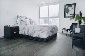A modern bedroom with a large bed, a nightstand, a desk, and a chair.