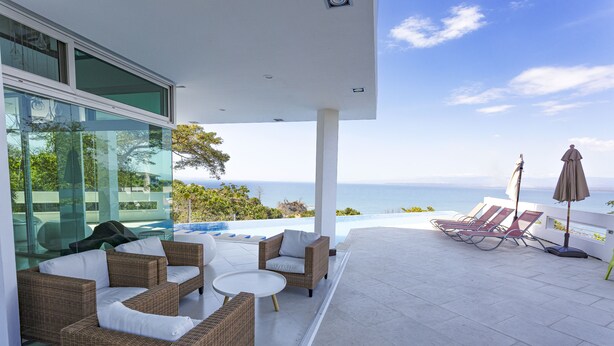A modern outdoor lounge area with wicker furniture, a pool, and a view of the ocean.