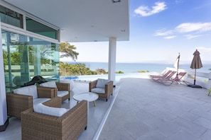 A modern outdoor lounge area with wicker furniture, a pool, and a view of the ocean.