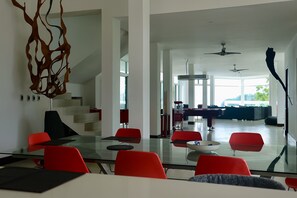 Ein modernes Interieur mit einem Glastisch, roten Stühlen, einem Billardtisch und einer Treppe, die zu einem Balkon führt.