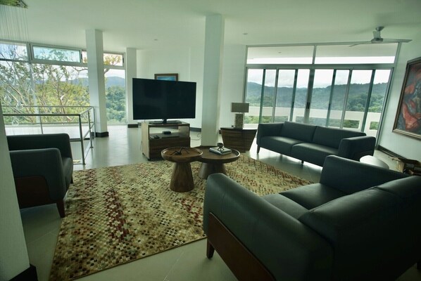 A modern living room with a large TV, comfortable seating, and a view of the outdoors.