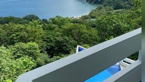 A balcony with a view of a coastal landscape, dense greenery, and a body of water.