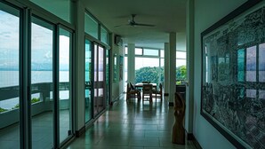 A spacious corridor with large windows, a dining area with chairs, and a ceiling fan.
