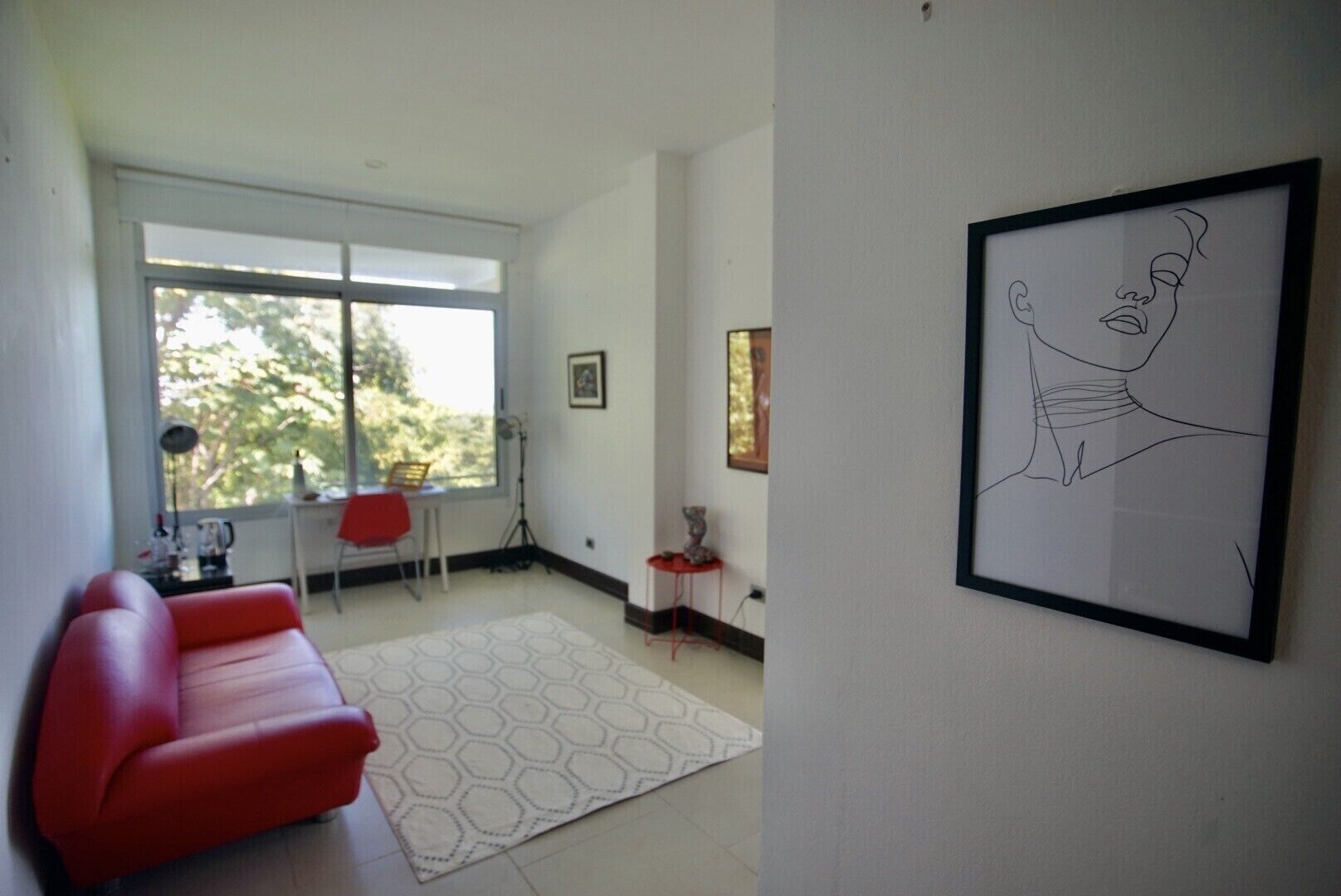 A modern living room with a red sofa, a white rug, and a large window offering a view of trees.
