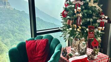 A room with a view of a castle, a Christmas tree, a green armchair, and a table with wrapped gifts.