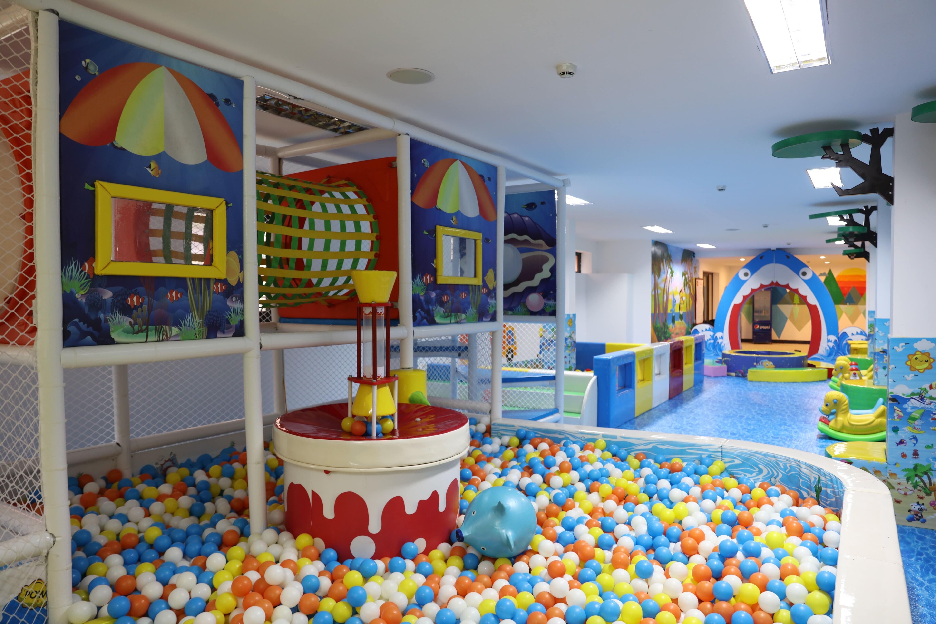 Un espace de jeux pour enfants avec une piscine à balles, des structures colorées et un toboggan.