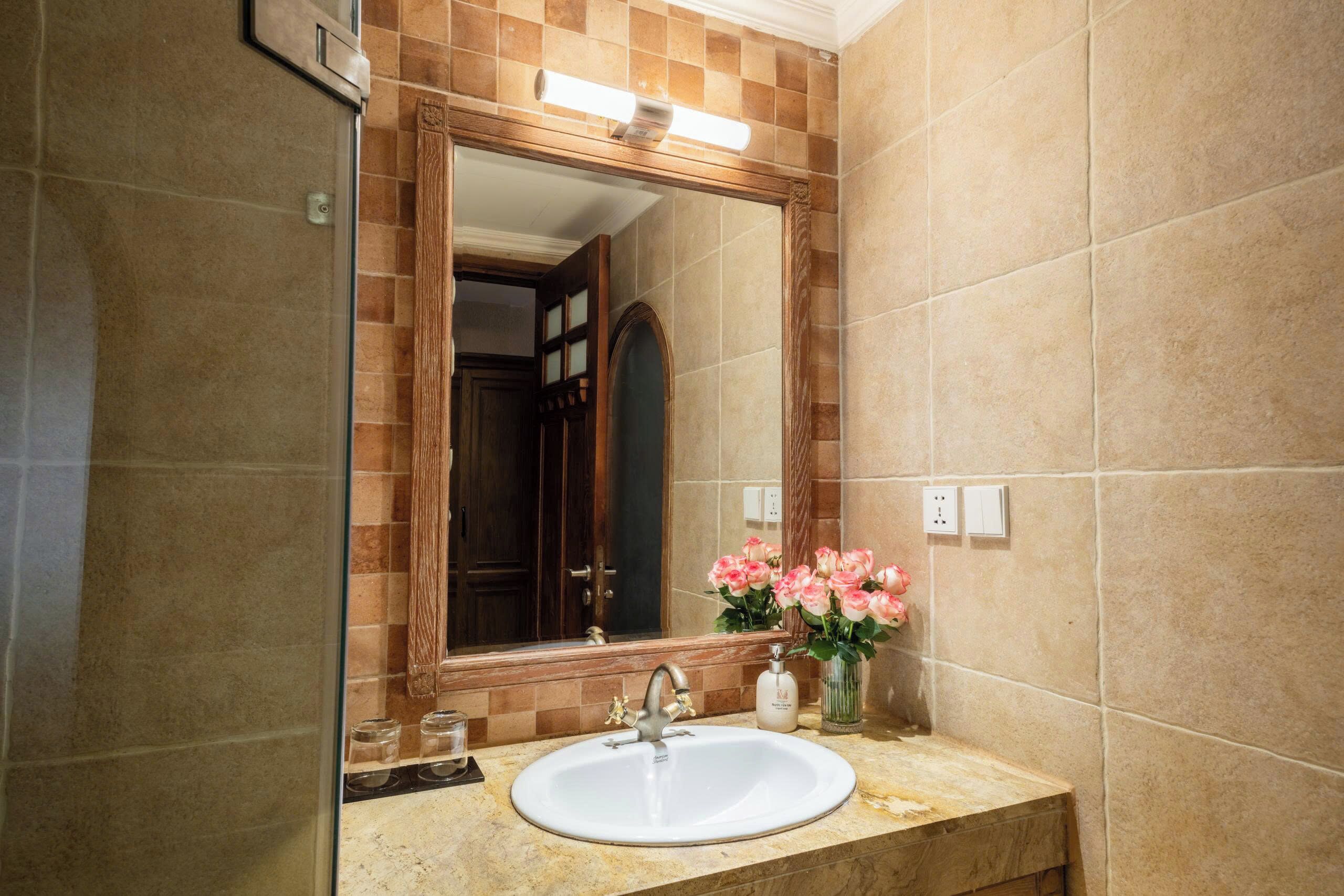 A bathroom with a white sink, a large mirror, and a vase with pink flowers.