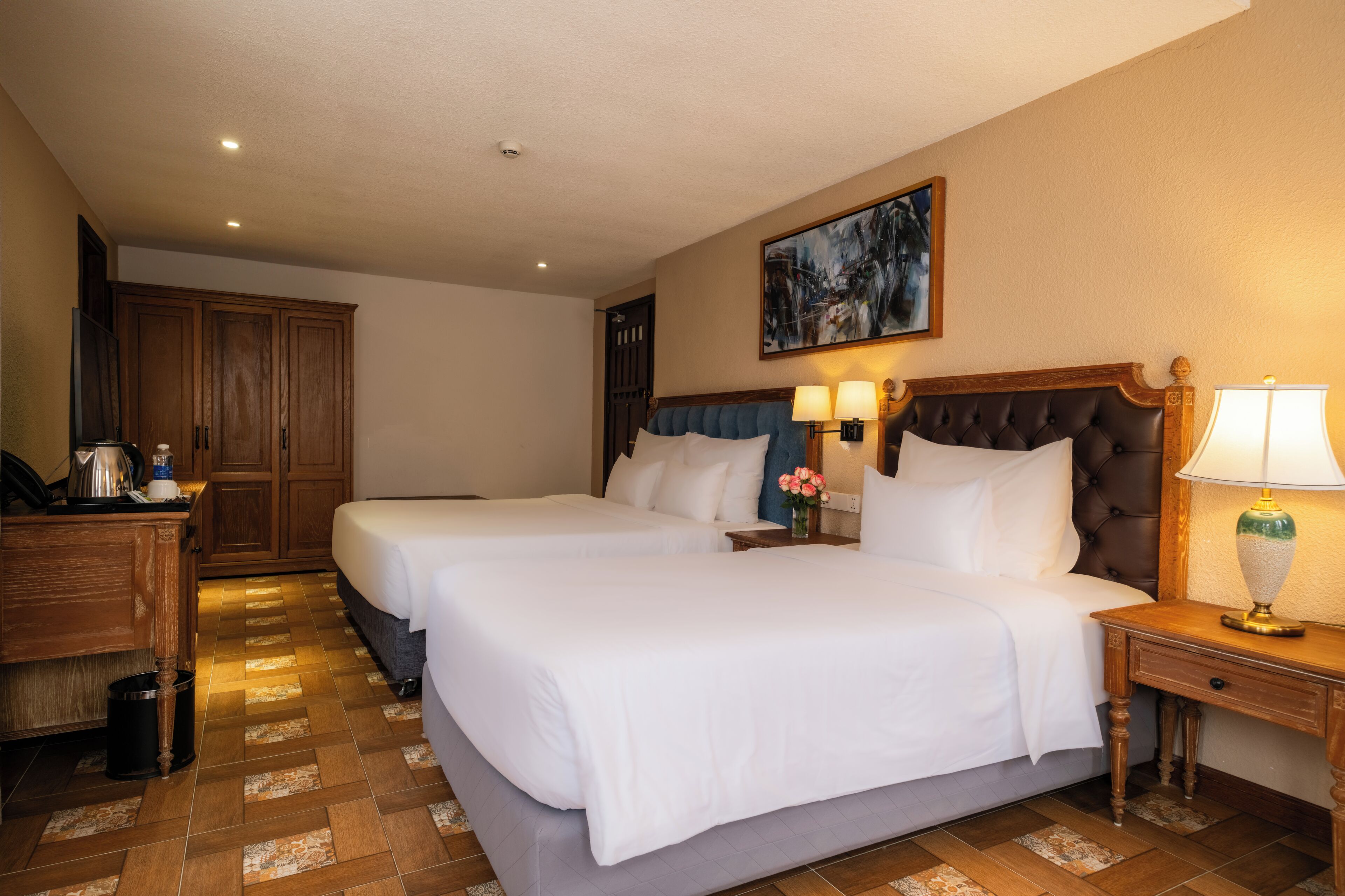 Habitación de hotel con dos camas, un escritorio y un cuadro en la pared.