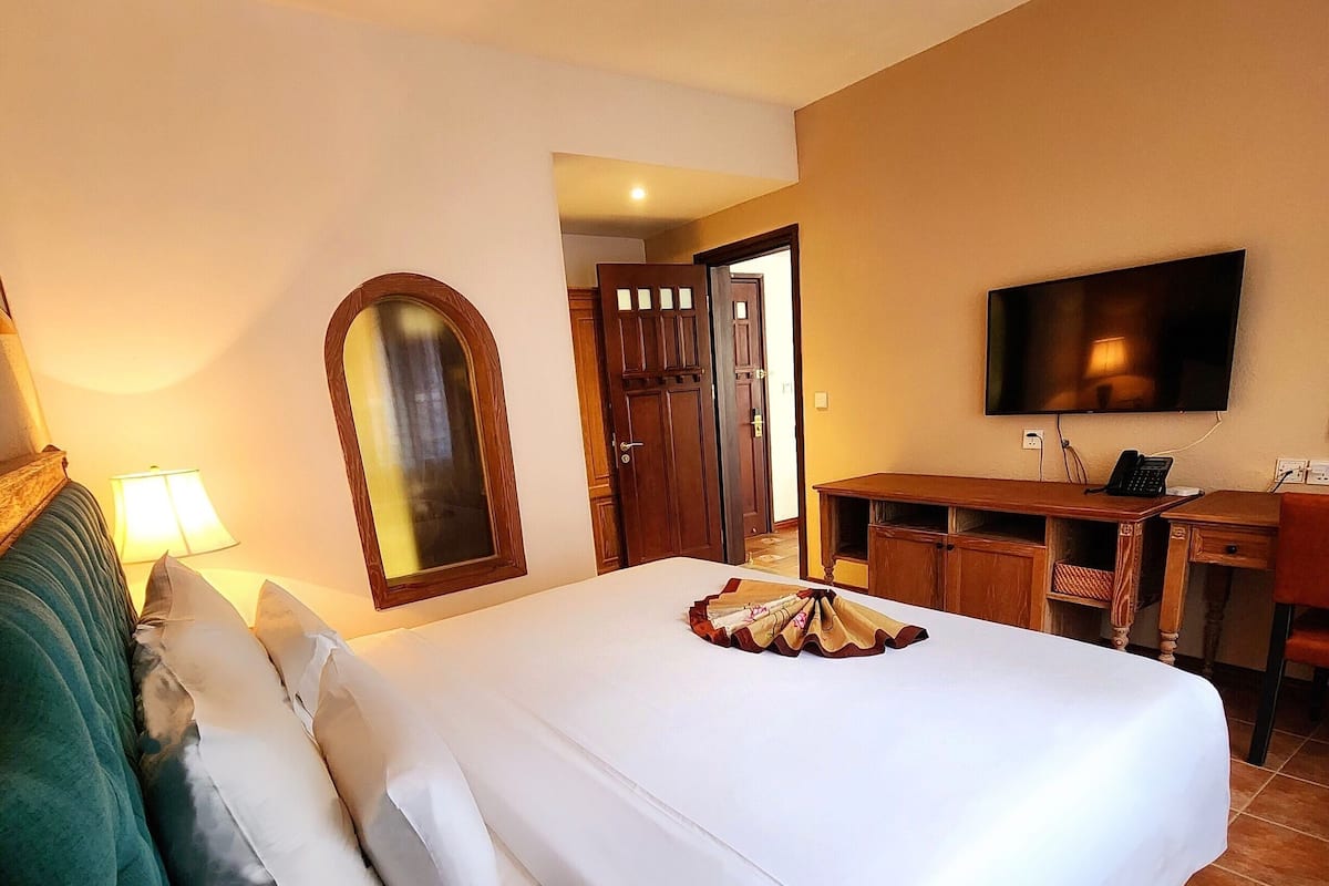 Une chambre d’hôtel avec un grand lit, un bureau, une télévision et une porte donnant sur une autre pièce.