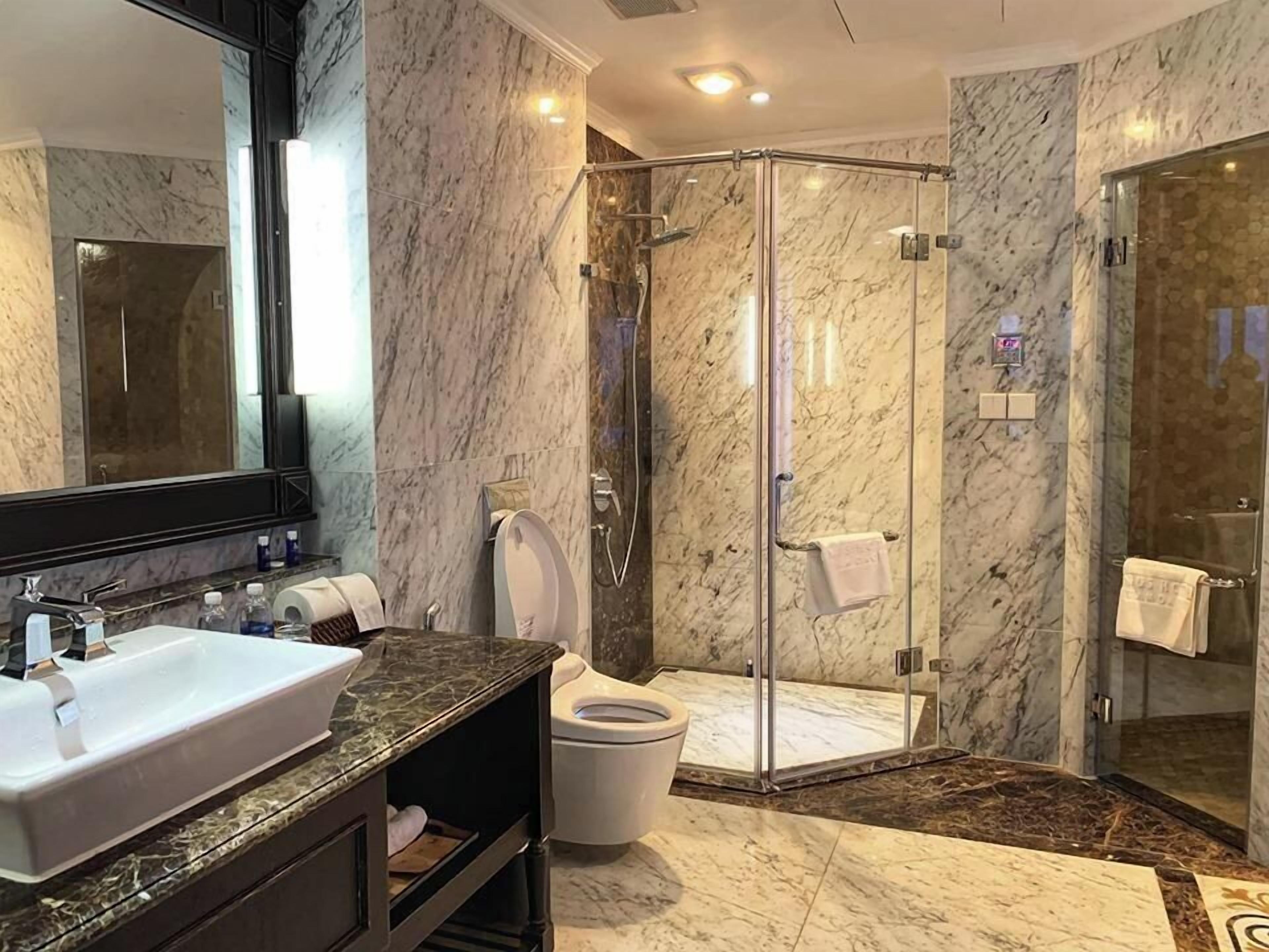Een moderne badkamer met een marmeren wastafel, toilet en een douche met glazen wanden.
