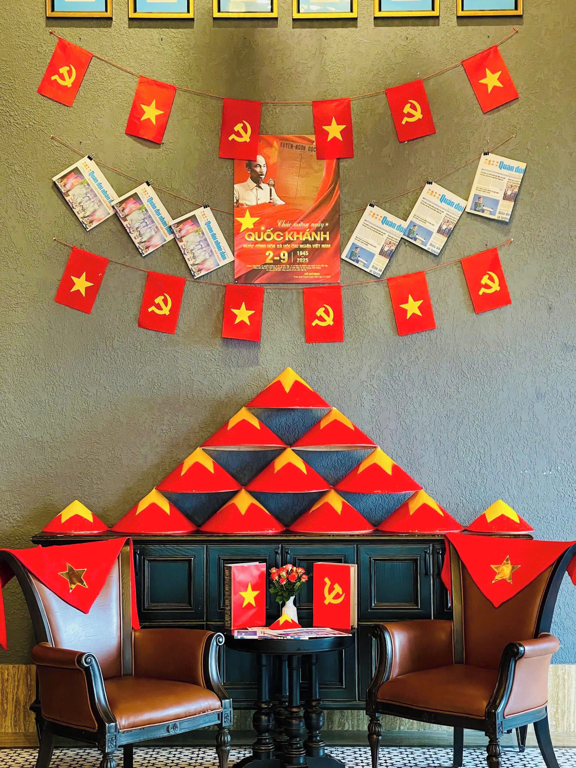 A room with a wall decorated with red flags and a poster. There are two chairs and a table with a vase of flowers.