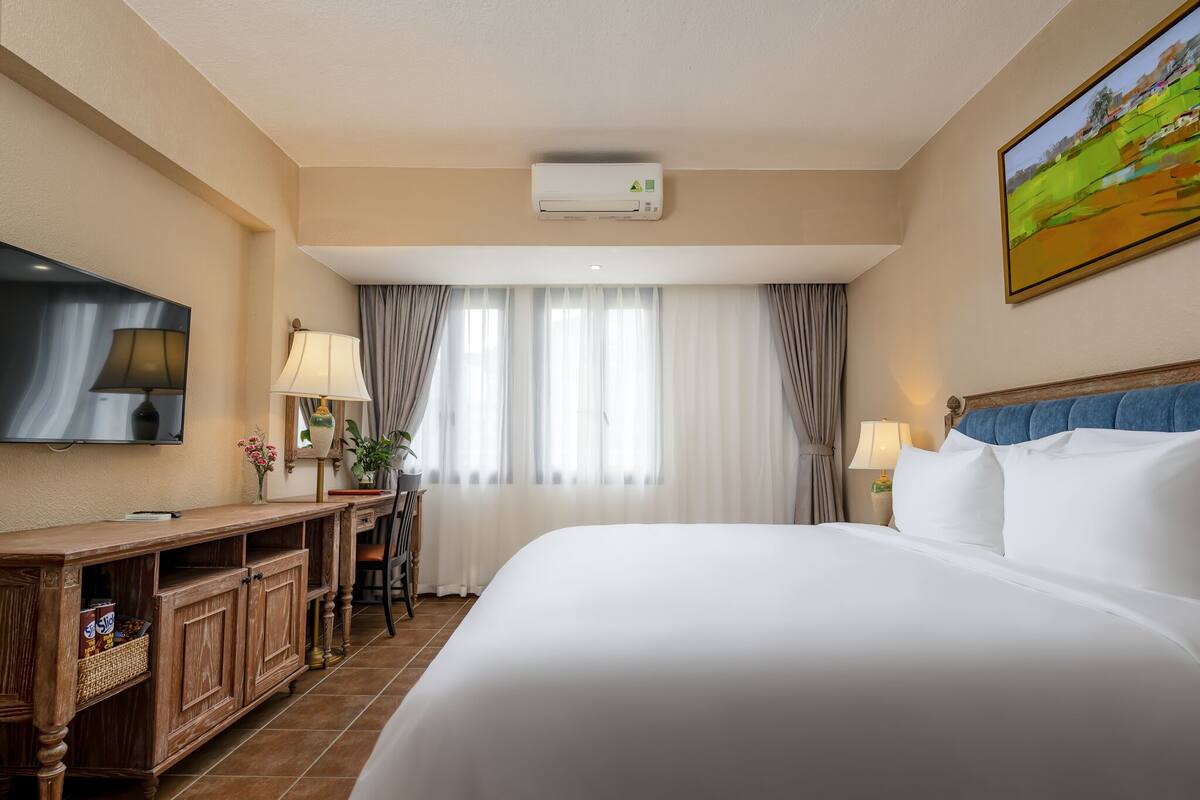 Une chambre d’hôtel avec un grand lit, un bureau avec une lampe, une télévision et un tableau au mur.