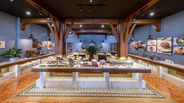 Un buffet proposant une variété de plats, avec un espace central pour se servir, le tout agrémenté de poutres en bois et d’un sol carrelé.