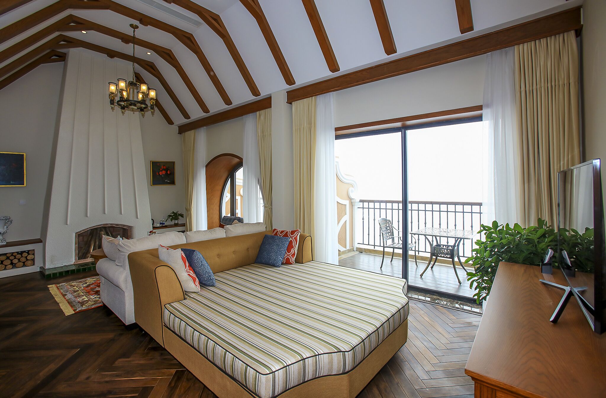 A spacious bedroom with a large bed, a balcony with a view, and a fireplace.