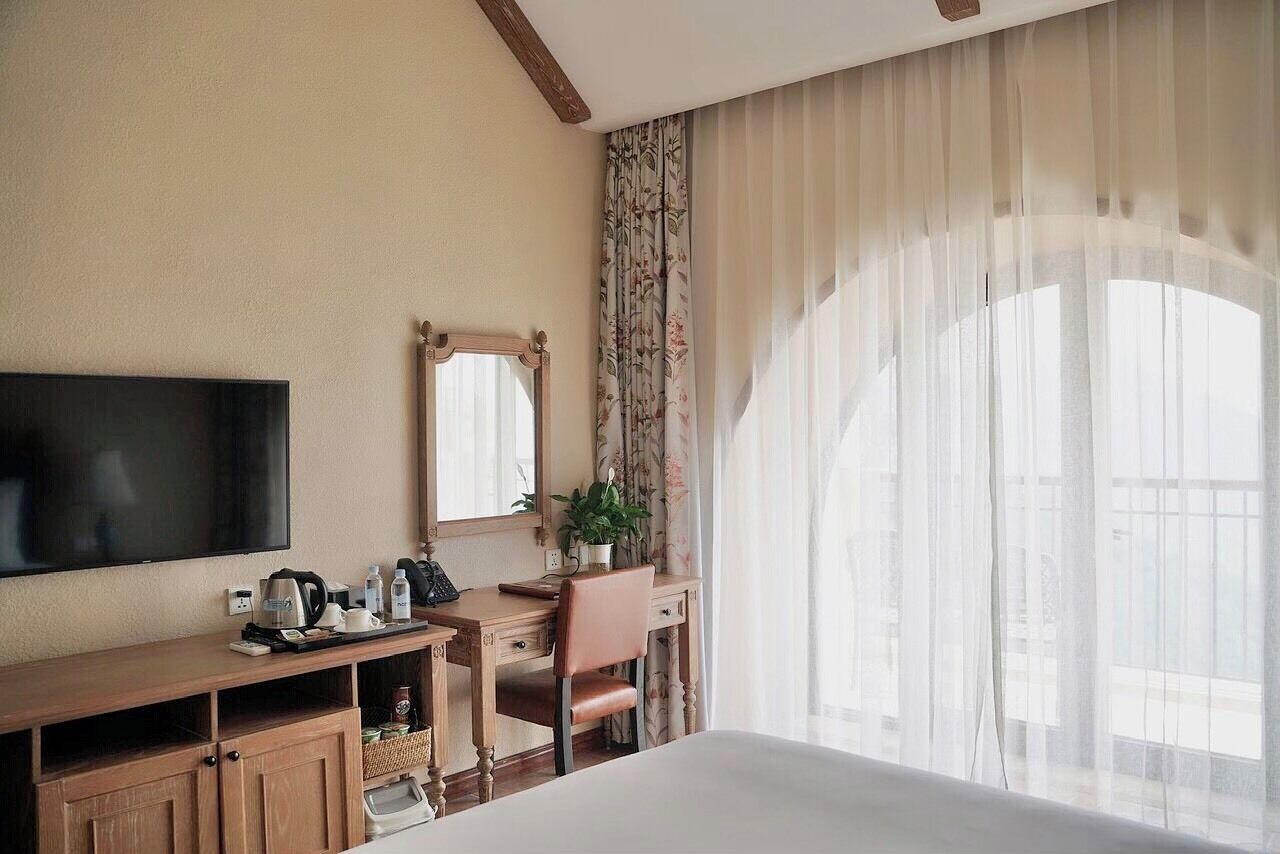 Une chambre d’hôtel comprenant un lit, une télévision, un bureau avec une chaise, un miroir et une fenêtre avec des rideaux.