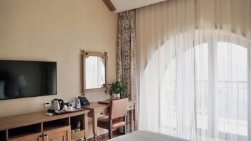 Une chambre d’hôtel comprenant un lit, une télévision, un bureau avec une chaise, un miroir et une fenêtre avec des rideaux.