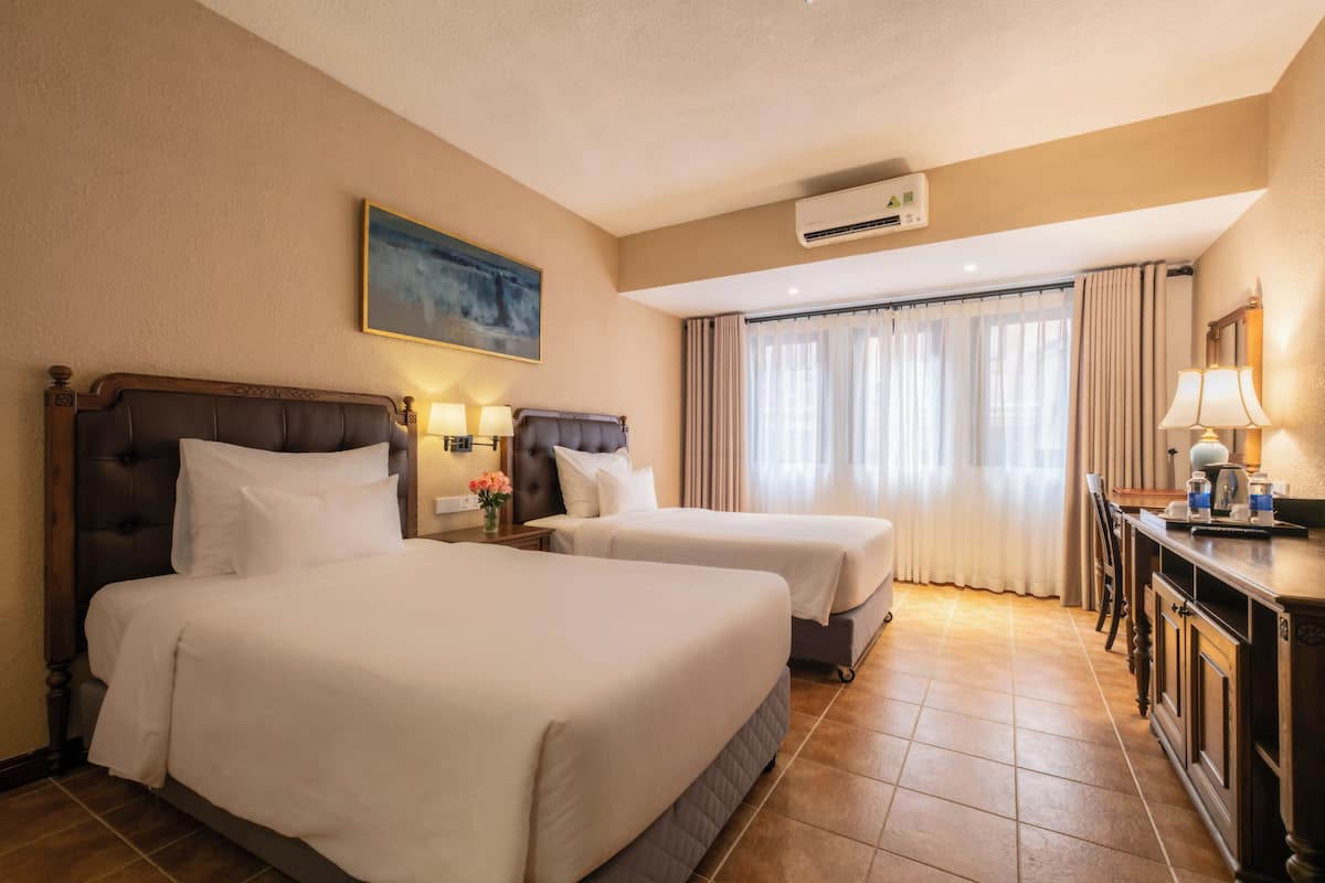 Une chambre d’hôtel avec deux lits, un bureau, une chaise, une lampe et un appareil de climatisation.